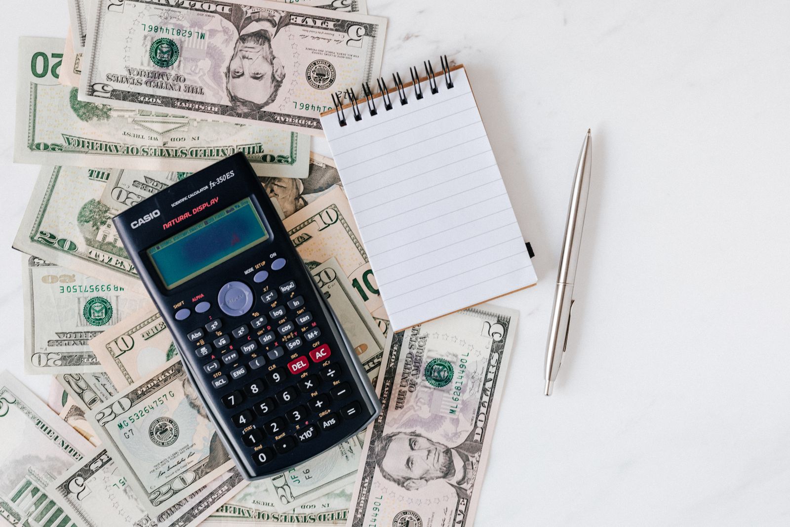 Calculator and notepad resting on a stack of dollar bills