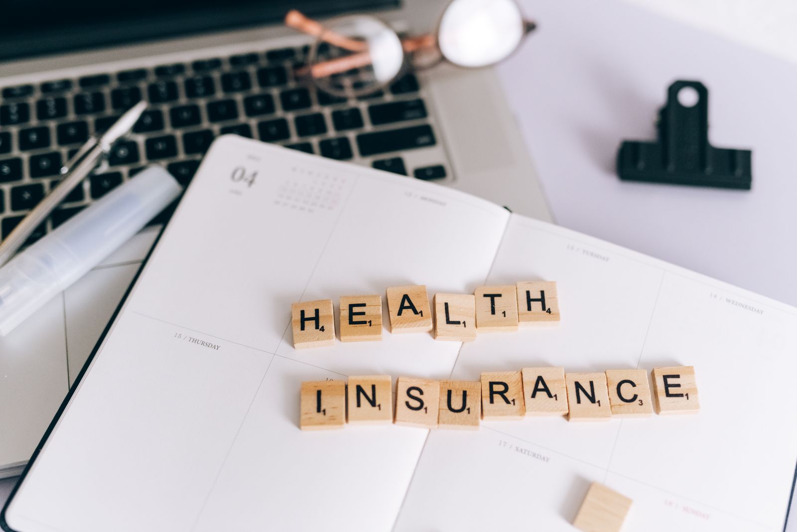 Scrabble tiles spelling Health Insurance on a planner next to a laptop